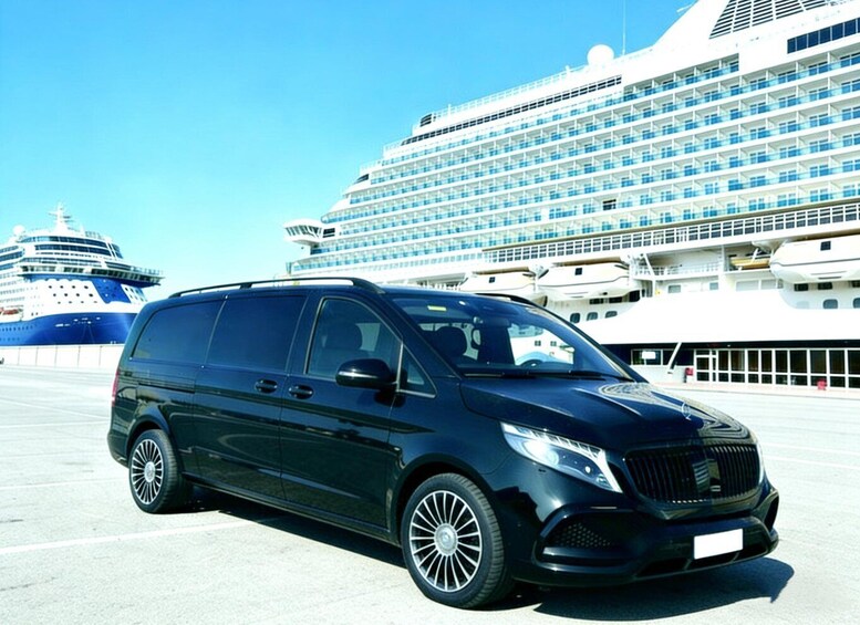A black minivan parked in front of a large cruise ship. 1
