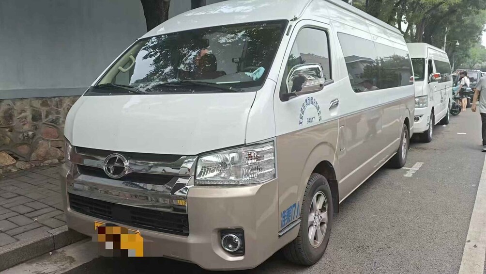 A white van parked on a street with a stone wall on one side and trees in the background. 2