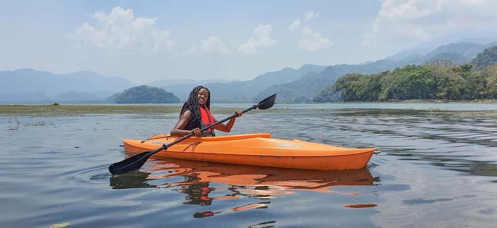 A person in an orange kayak on calm water with mountains in the background. 3