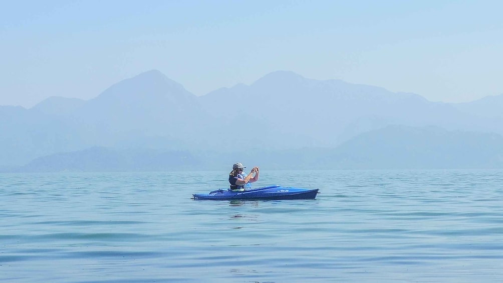 A person in a blue kayak on calm water with mountains in the background. 5