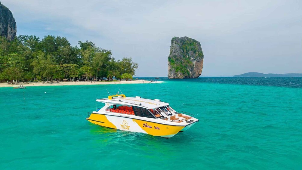 Ein gelbes Boot namens 'Lotus Turia' auf türkisblauem Wasser mit Strand und einer großen Felsformation im Hintergrund. 3