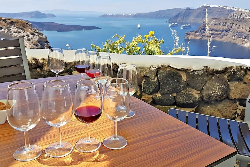 A table with wine glasses and a bowl of bread, overlooking a scenic coastal view with cliffs and the sea. 3