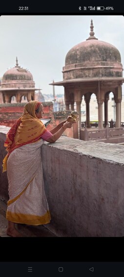 Una persona vestida con traje tradicional, sosteniendo un objeto pequeño, observa un edificio histórico con cúpulas. 4