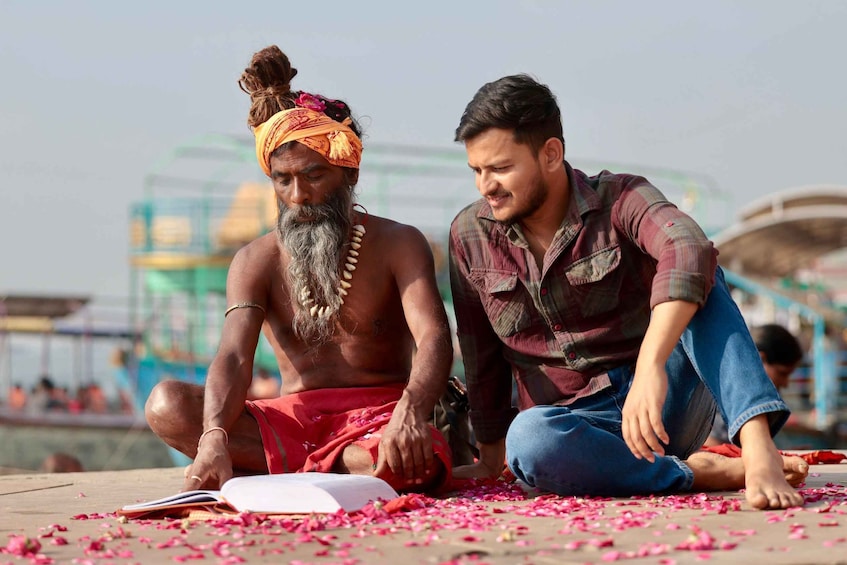 Two individuals sitting on the ground with a book and scattered flower petals. 4