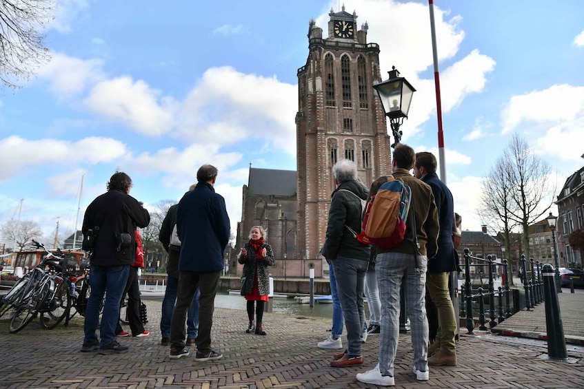 A group of people standing on a cobblestone path, looking at a tall brick tower with a clock. 1