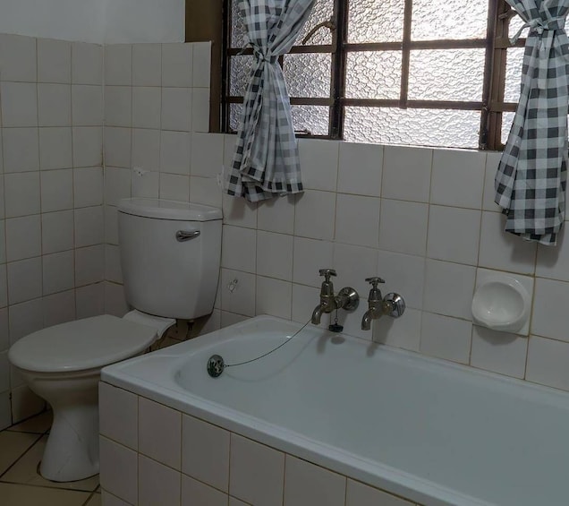 A bathroom with a toilet, a bathtub, and a window with curtains. 5
