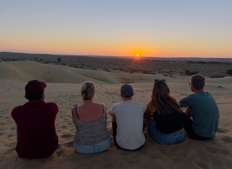 Four people sitting on sand dunes at sunset. 1