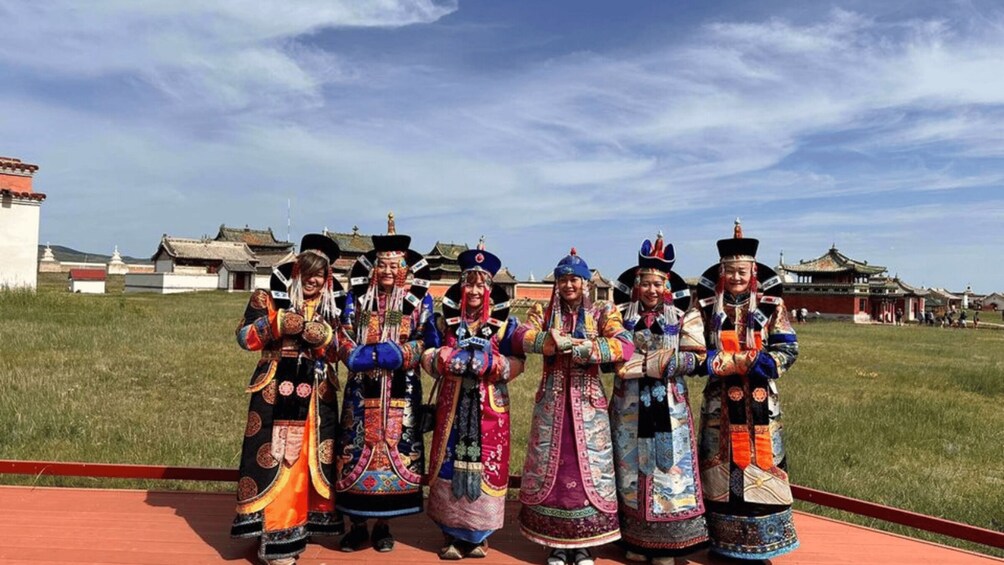 A group of people in traditional attire standing in a grassy field with buildings in the background. 5