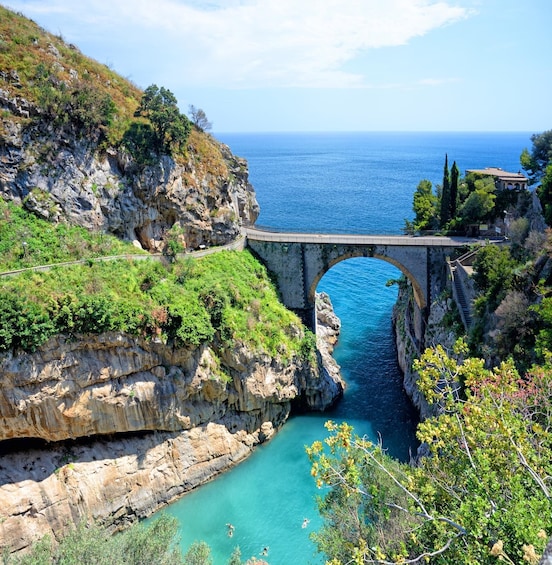 A coastal bridge over a turquoise sea, surrounded by rocky cliffs and greenery. 5