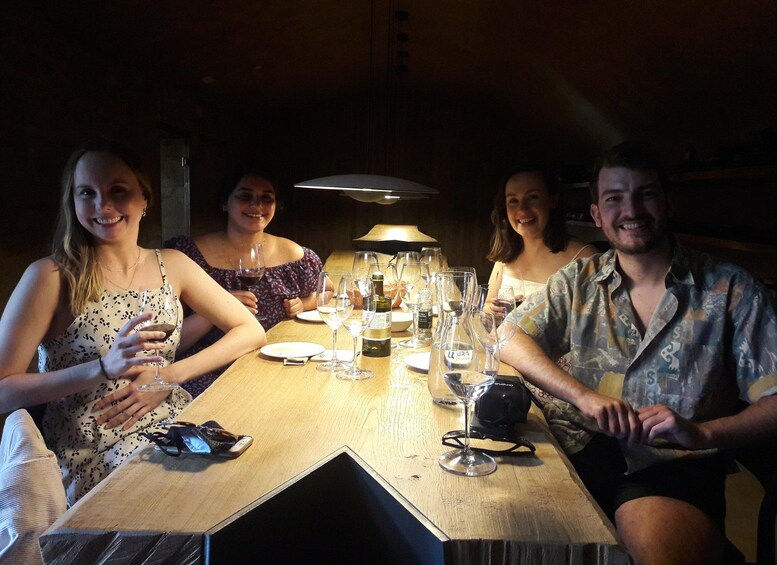 Four people sitting at a wooden table with wine glasses and bottles. 3