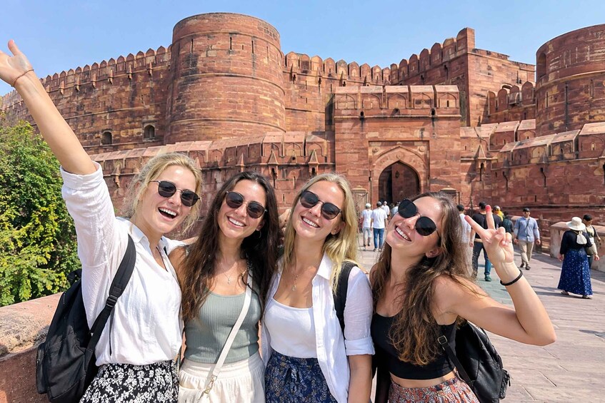 A group of people posing in front of a large, historic fort with red brick walls and arched windows. 5