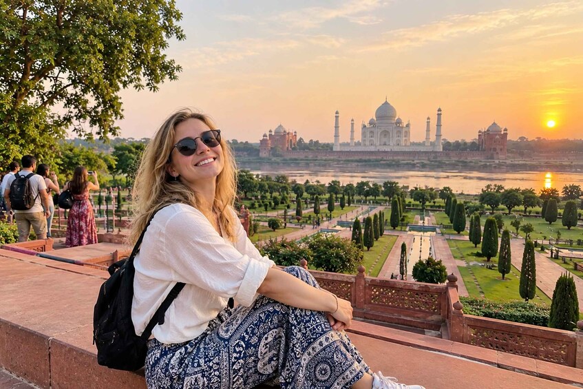 A person sitting on a ledge overlooking the Taj Mahal with the sun setting in the background. 4
