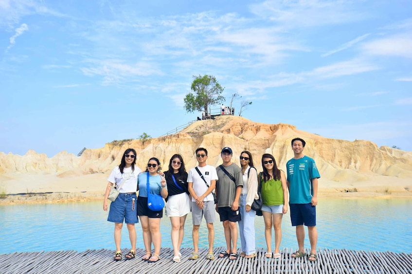 A group of people standing on a wooden dock by a calm body of water with a rocky hill in the background. 5