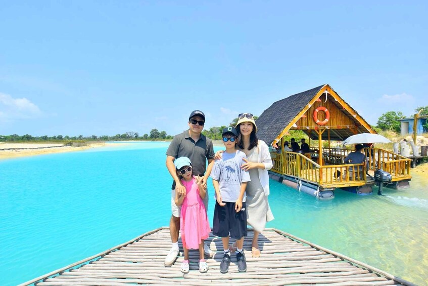 A family on a wooden dock with a clear blue sea and a wooden structure with a lifebuoy in the background. 1