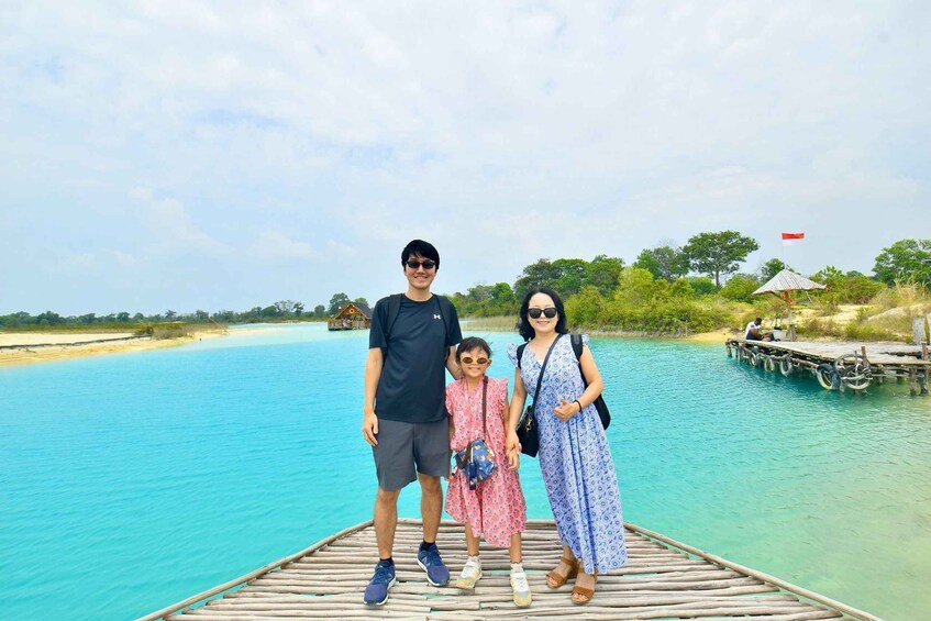 A family standing on a wooden dock over turquoise water with a beach and trees in the background. 4