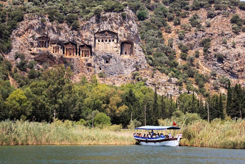Un barco con turistas en un lago, acantilados con ruinas antiguas al fondo. 2