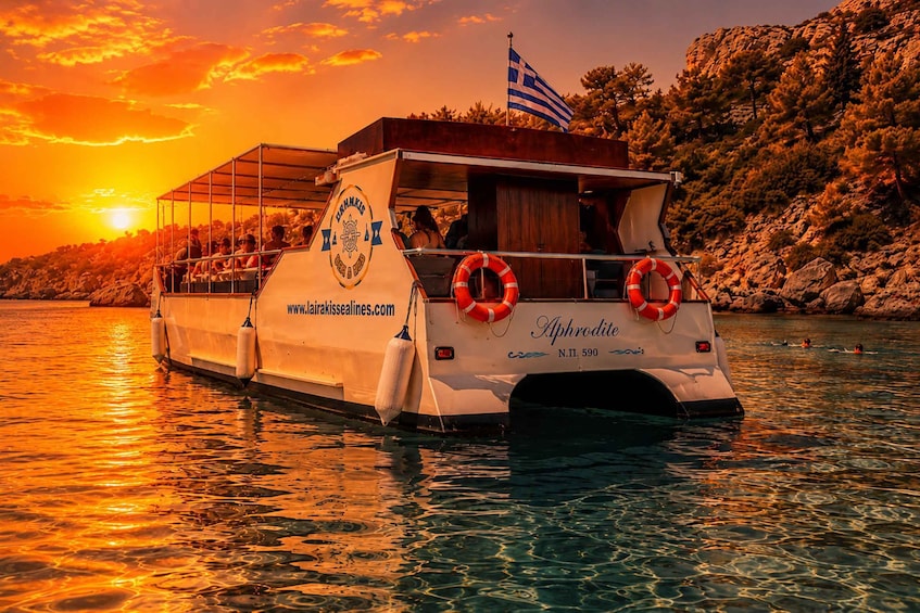 A boat named Aphrodite anchored near rocky shores during sunset. 1
