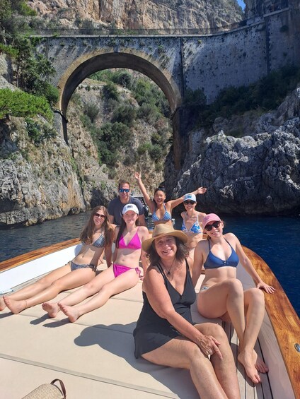 A group of people on a boat near a stone bridge over water with rocky cliffs. 4