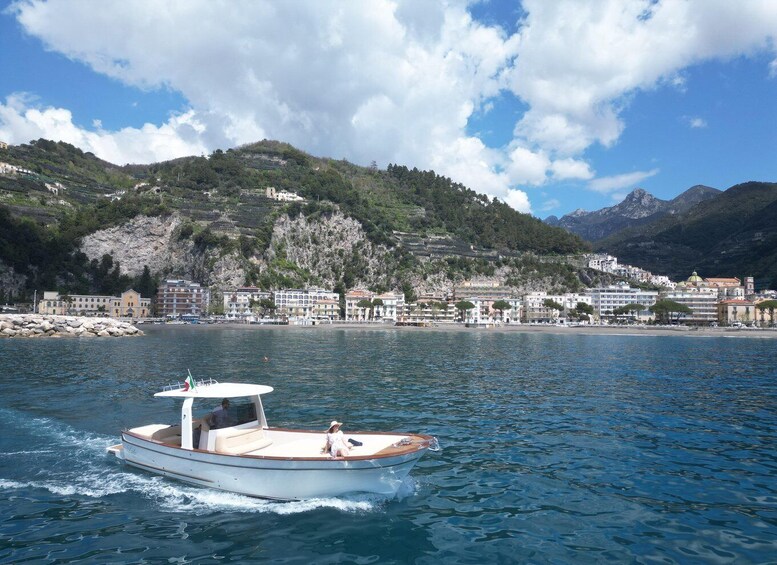 A boat on calm water with a coastal town and mountains in the background. 1