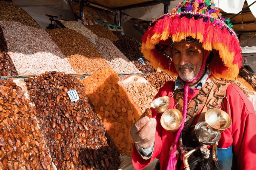 A person in traditional attire at a market stall with various nuts and grains. 1