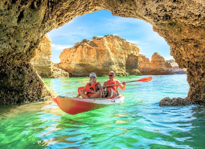 Two people kayaking through a natural arch formation surrounded by clear blue waters and rocky cliffs. 4