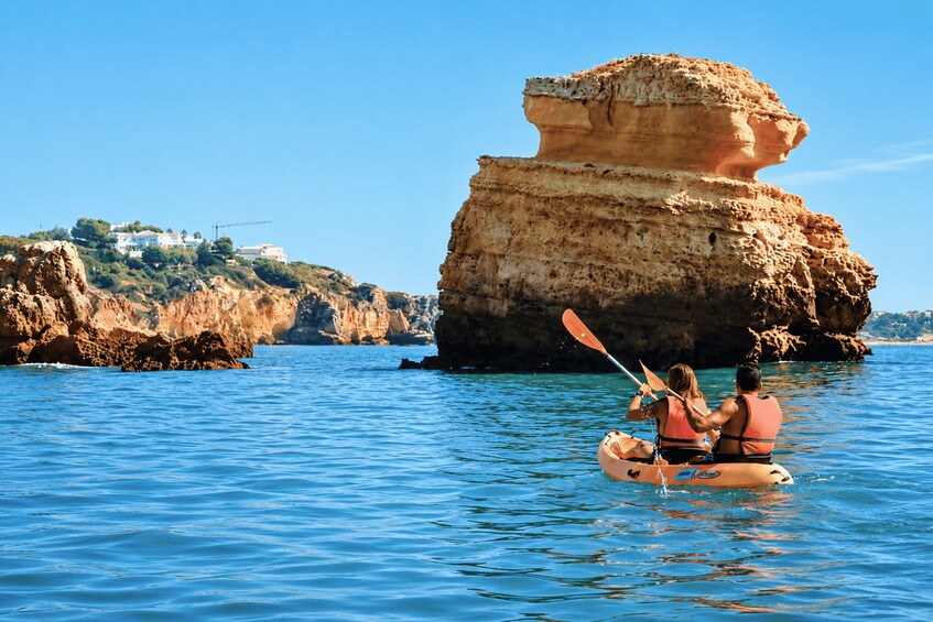 A couple kayaking on calm waters with a large rock formation in the background. 2