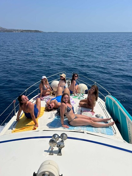 A group of people sunbathing on a boat with a clear blue sea and distant land in the background. 1