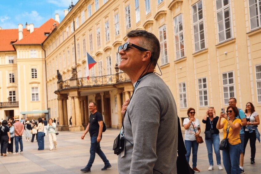 A man walking in a square with historic buildings and a flag. 3
