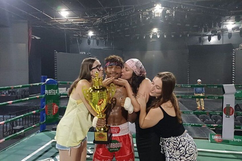 A boxing ring with a trophy, a person in red shorts, and a person in a black tank top. 2