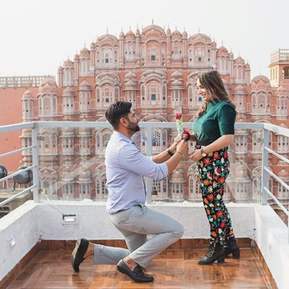 A man kneeling on a balcony with a woman holding a bouquet of flowers. 4