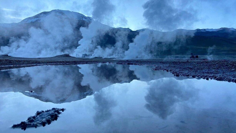 A lake reflecting mountains and steam rising from the ground. 2