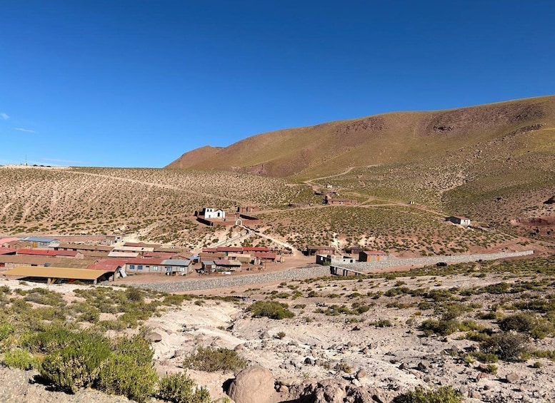 A desert landscape with sparse vegetation, a small settlement with buildings, and a hill in the background. 5