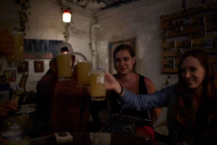 People toasting with drinks in a dimly lit bar with wooden shelves and a rustic decor. 2