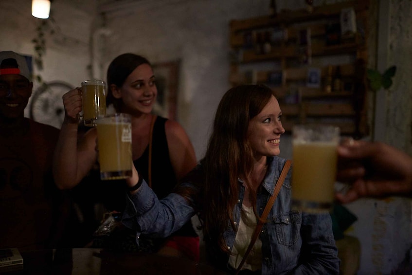 People toasting with drinks in a dimly lit room with a bookshelf in the background. 4