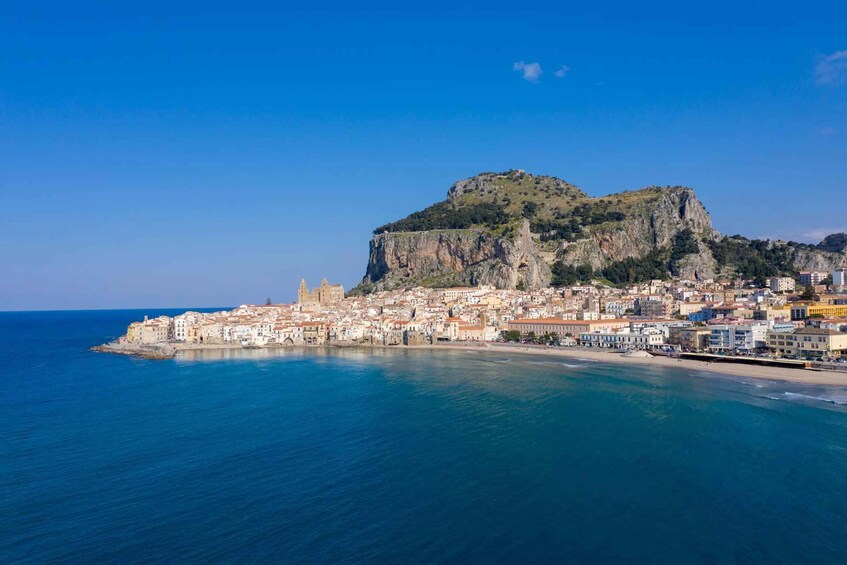 A coastal town with a prominent hilltop fortress, a historic church, and a clear blue sea. 3
