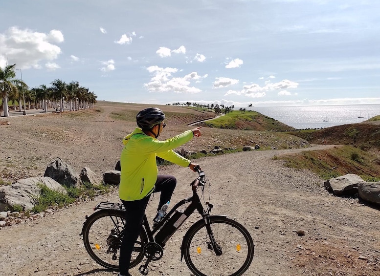 Una persona in bicicletta su un sentiero sterrato, con palme e vista sull'oceano. 1