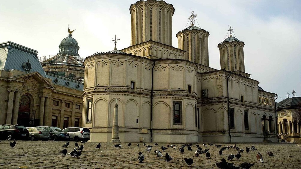 A historic church with multiple domes and towers, surrounded by pigeons on a cobblestone square. 2