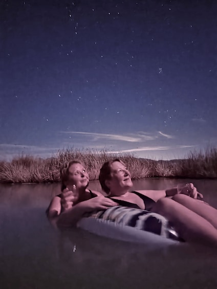 Two people floating on a raft in a body of water with a starry night sky above. 2
