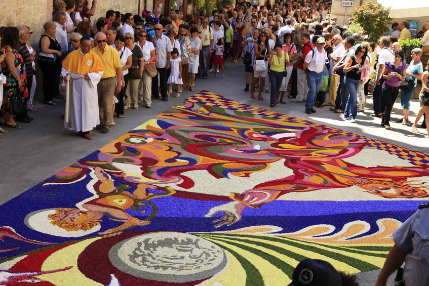 A crowd of people gathered around a colorful carpet with intricate designs. 3
