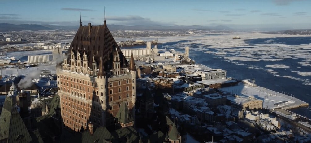 A historic building with a pointed roof, surrounded by snow-covered streets and a frozen river. 1
