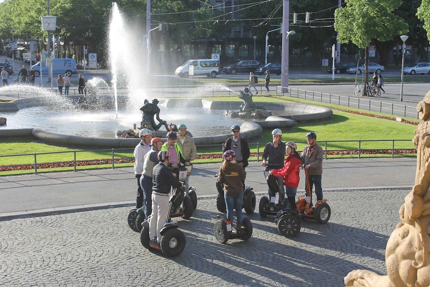 A group of people on segways around a fountain in a public square. 4