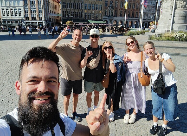 Ryhmä ihmisiä poseeraa valokuvaa varten julkisella aukiolla, jonka taustalla näkyy historiallisia rakennuksia. 3