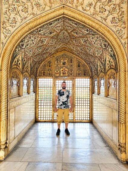 A man standing in a hallway with ornate golden arches and intricate floral patterns on the ceiling. 2