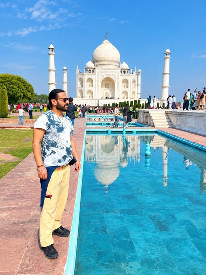 A person standing in front of the Taj Mahal with a reflection in the pool. 4