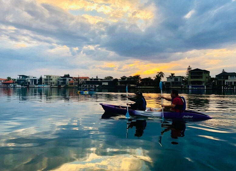 A sunset over a calm body of water with two canoes, one purple and one blue, with people paddling. 3