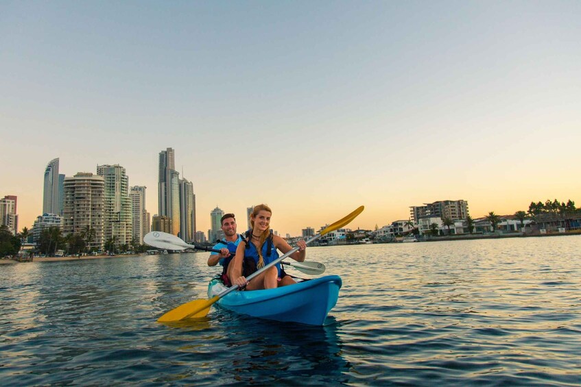 Two people kayaking on a body of water with a city skyline in the background. 5