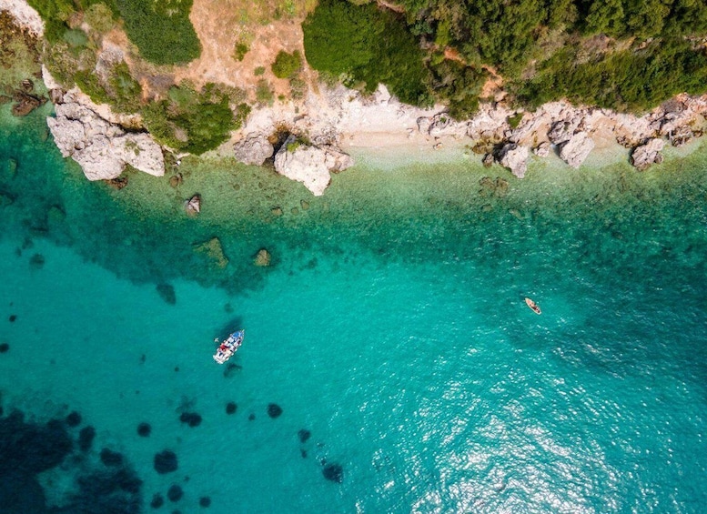 An aerial view of a turquoise coastal area with clear waters, rocky outcrops, and a small boat. 2