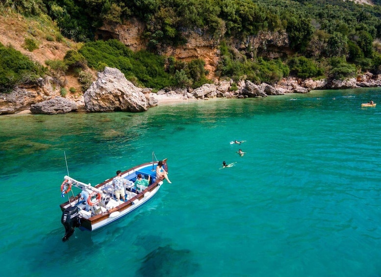 A boat with passengers and swimmers in a clear turquoise sea, surrounded by rocky cliffs and greenery. 4