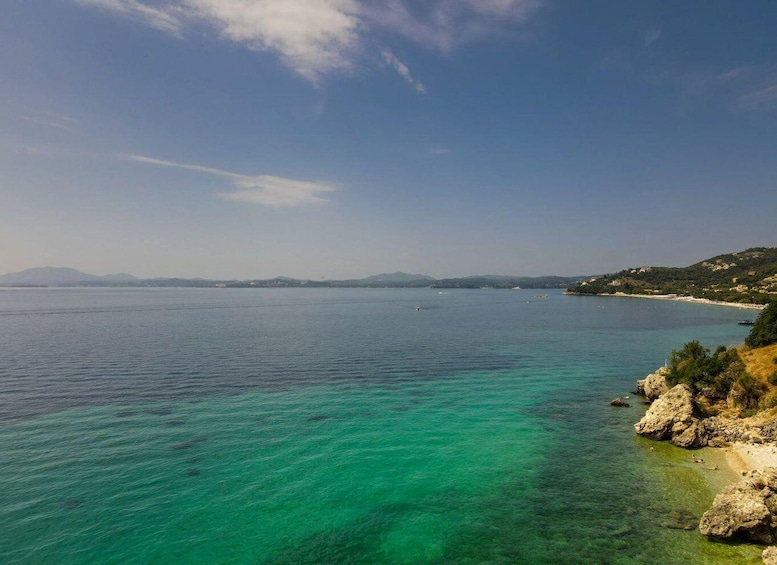 A coastal landscape with clear turquoise waters, rocky shoreline, and distant mountains under a clear sky. 5