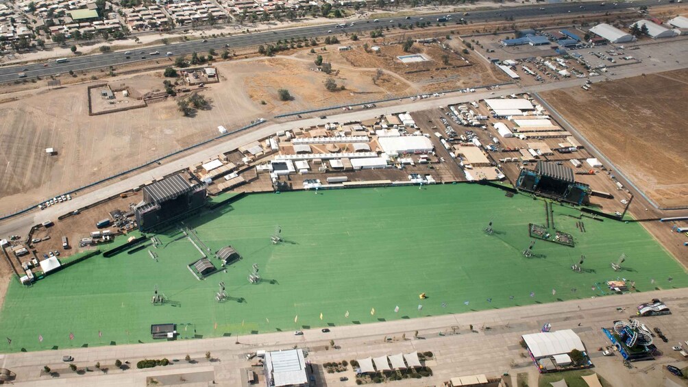 An aerial view of a stadium with a green field, surrounded by temporary structures and vehicles. 5